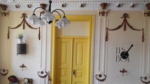 A room with a yellow door, decorative wall hangings, a white chair with a book, and a remote control on a couch. - Refuge in Santa Marta Hostel (Lisbon)