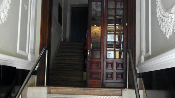 A grand staircase with a wooden door and glass panels, leading to a room with a chandelier. - Refuge in Santa Marta Hostel (Lisbon)