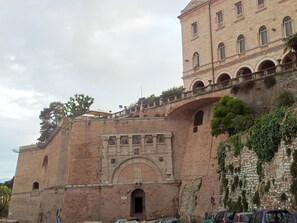 Un edificio histórico con una gran entrada en arco, un balcón con barandilla y un muro de ladrillo cubierto de vegetación.