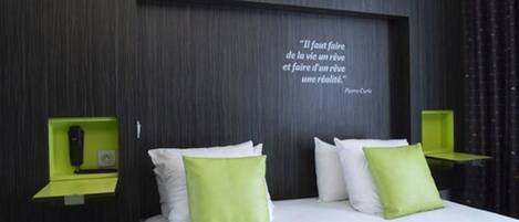 A modern hotel room with a large bed, green nightstands, and a quote on the wall.