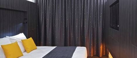 A hotel room with a bed, two pillows, a dark curtain, and a window.