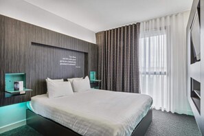 A modern hotel room with a large bed, a wall-mounted quote, a bedside table with a lamp, and a window with curtains. - Akena Nantes Atlantis (Saint-Herblain)