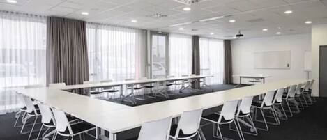 Un salón de conferencias con una larga mesa, sillas blancas y alfombra negra.