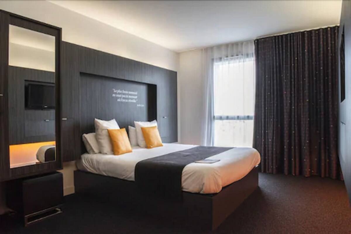 A modern hotel room with a large bed, a flat-screen TV, and a large mirror.