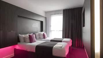 Une chambre d’hôtel moderne avec deux lits, une grande fenêtre et un mur revêtu de panneaux en bois foncé.