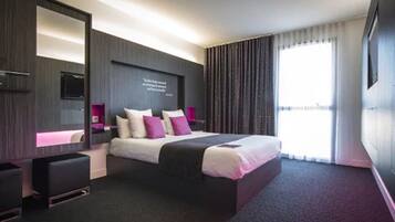 Habitación de hotel moderna con una cama grande, un televisor de pantalla plana montado en la pared, una mesita de noche y un ventanal con cortinas.