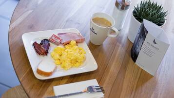 Un plat d'esmorzar amb ous barrejats, bacon i torrades, una tassa de cafè i un menú sobre una taula de fusta.
