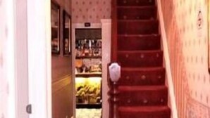 A narrow hallway with a red carpet leading to a staircase with a chandelier. - Parkfield Hotel (Blackpool)