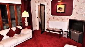 A living room with a white sofa, red carpet, a lamp, a television, and a framed picture on the wall. - Parkfield Hotel (Blackpool)