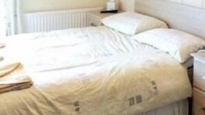 A bedroom with a bed, a nightstand, and a wall-mounted light fixture. - Parkfield Hotel (Blackpool)