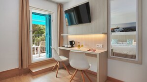 Una habitación de hotel moderna con un escritorio de madera, dos sillas blancas, un televisor de pantalla plana montado en la pared y un gran ventanal con vistas al exterior.