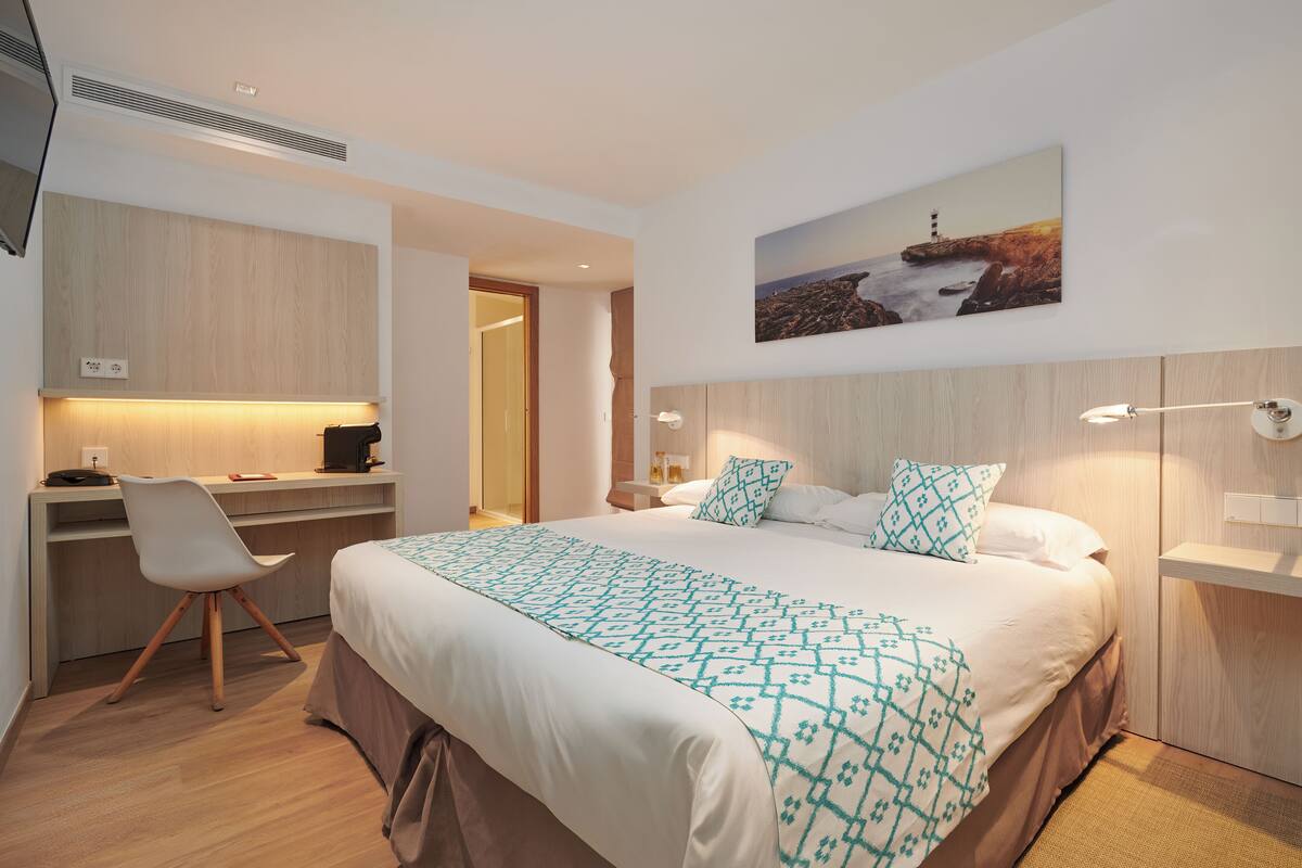 Habitación de hotel moderna con una cama grande, un escritorio con silla, una mesita y un estante en la pared.