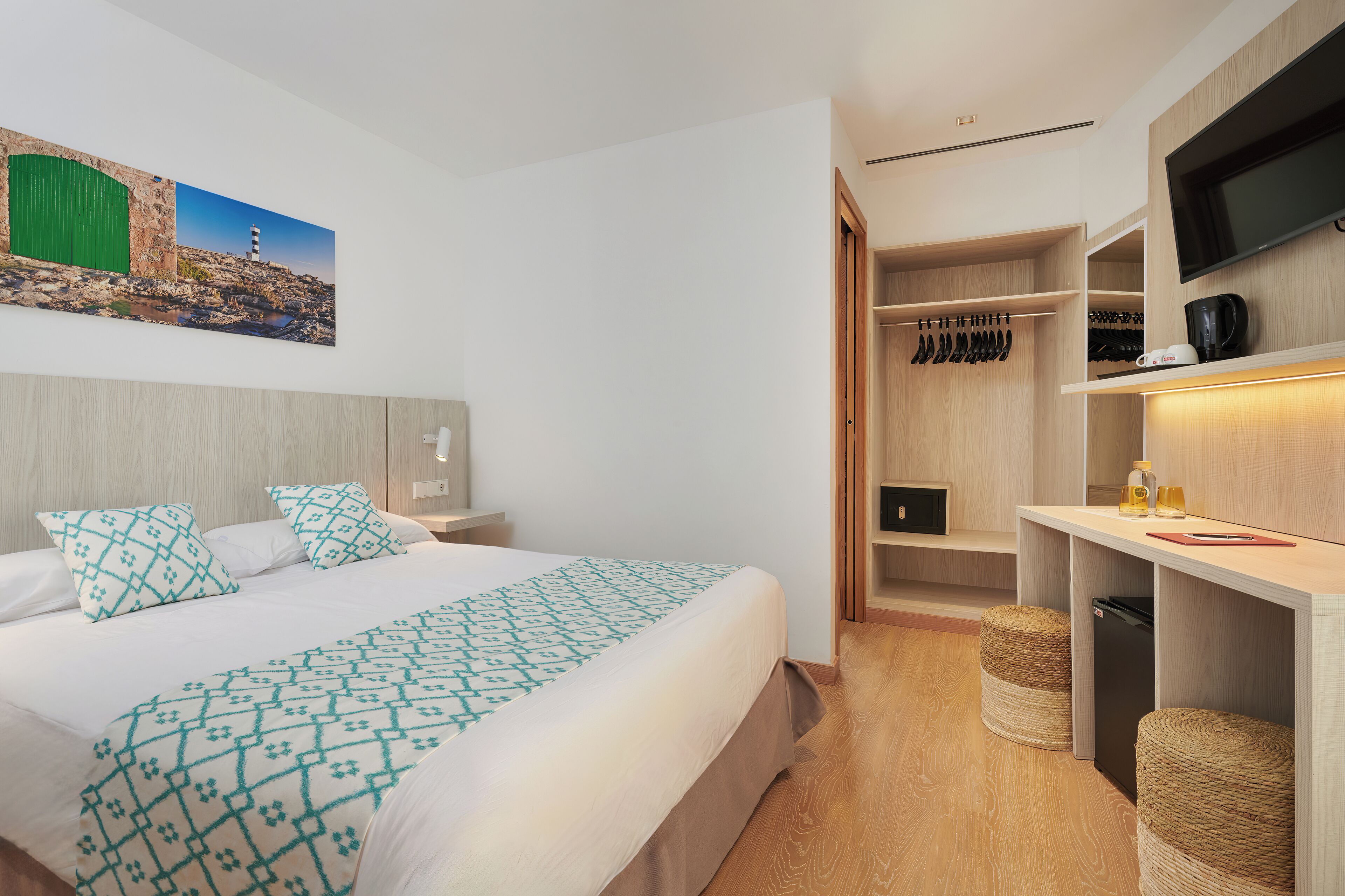 Een moderne hotelkamer met een groot bed, een inloopkast, een televisie en een schilderij van een kustlandschap.