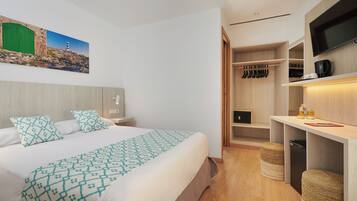 Een moderne hotelkamer met een groot bed, een inloopkast, een televisie en een schilderij van een kustlandschap.
