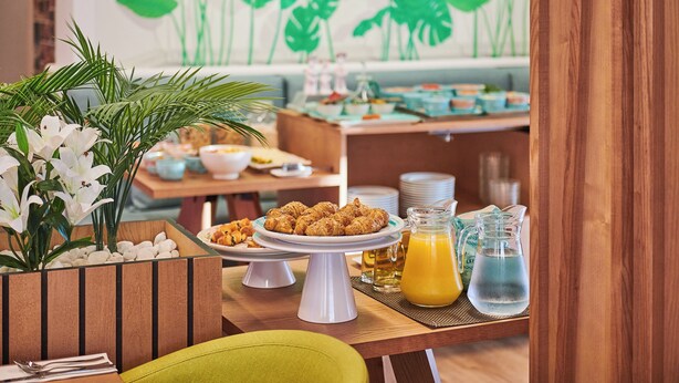 Un bufé de desayuno con diferentes platos, una jarra de zumo de naranja y una planta decorativa.