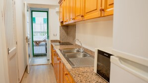 Cocina estrecha con armarios de madera, encimera de granito, pileta de acero inoxidable y microondas integrado.