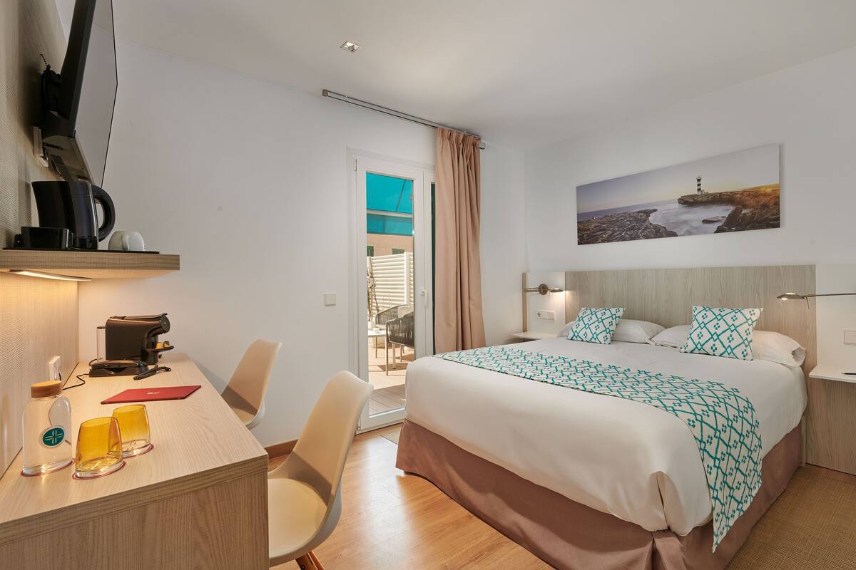 Habitación de hotel con cama, escritorio, silla y un cuadro de un faro.