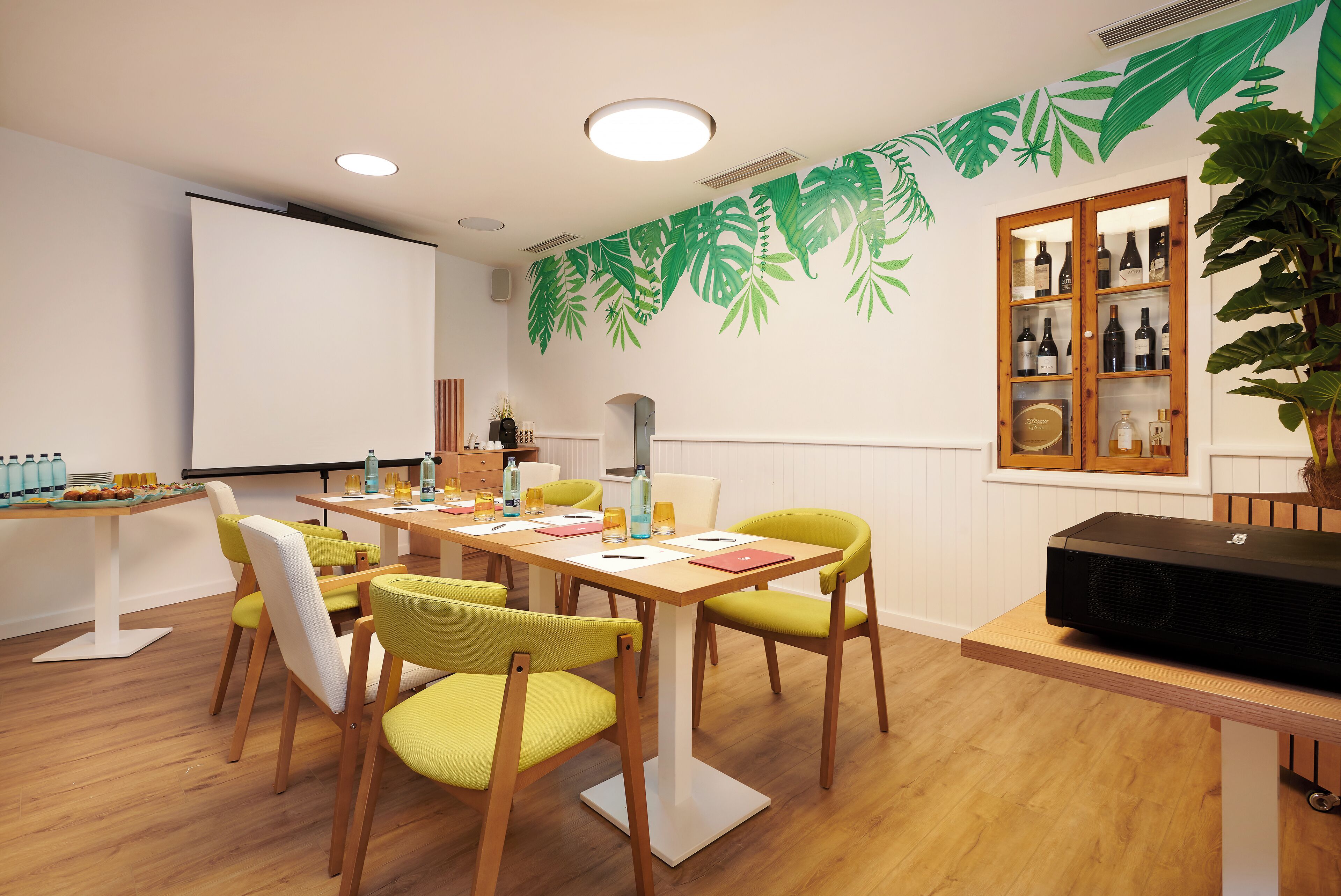 A conference room with a whiteboard, a projector, and a cabinet with bottles.