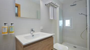 Un baño moderno con un lavabo blanco, tocador de madera, cabina de ducha de vidrio y dos botellas de artículos de aseo en la pared.