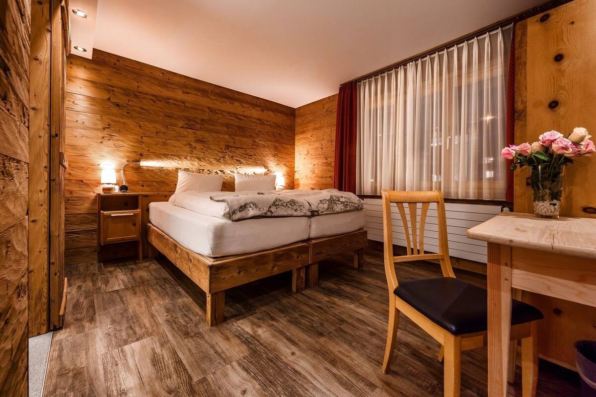A wooden room with a bed, bedside tables, a chair, and a table.