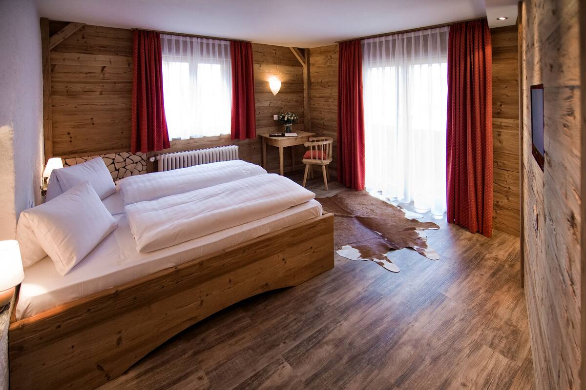 A wooden room with a large bed, a desk, and a cowhide rug.