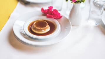 Un dessert servi sur une assiette blanche, accompagné d’un verre d’eau et d’une fleur rose en arrière-plan.