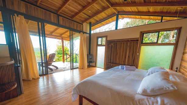 A bedroom with a large bed, wooden flooring, and a view through a glass door. - Hotel Mystica (Santa Rosa)