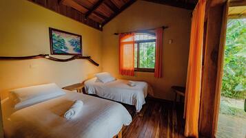 Una habitación con dos camas, suelo de madera, un cuadro en la pared y una ventana con cortinas.