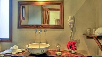 Un baño con espejo de marco de madera, un lavabo blanco con diseño floral, una toalla, un secador de pelo y un florero con flores rosas.