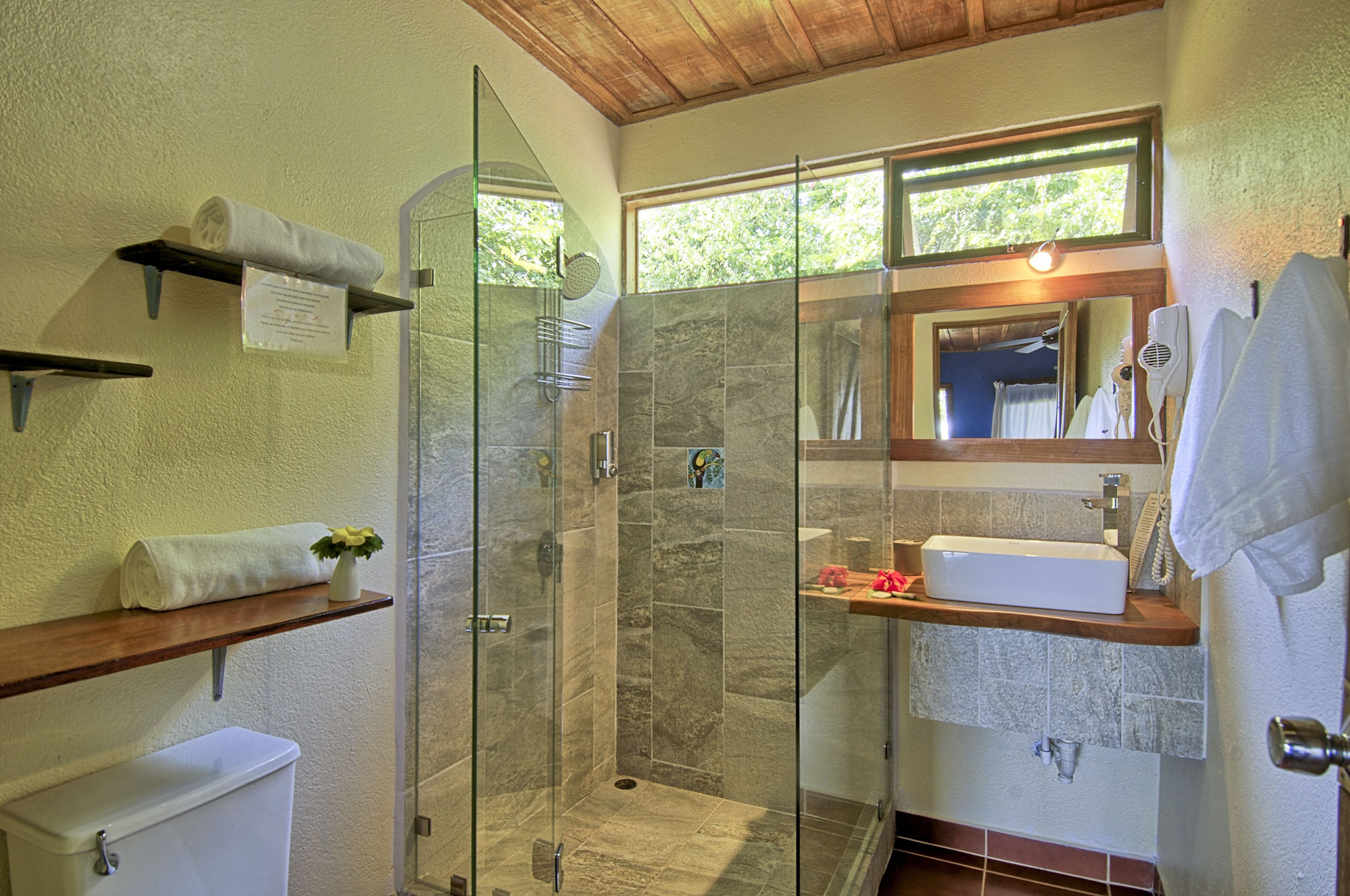 A modern bathroom with a glass-enclosed shower, a white sink, and a wooden shelf.