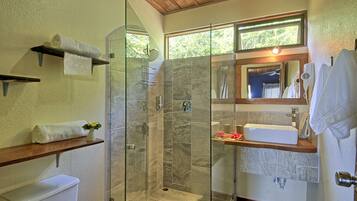 A modern bathroom with a glass-enclosed shower, a white sink, and a wooden shelf.