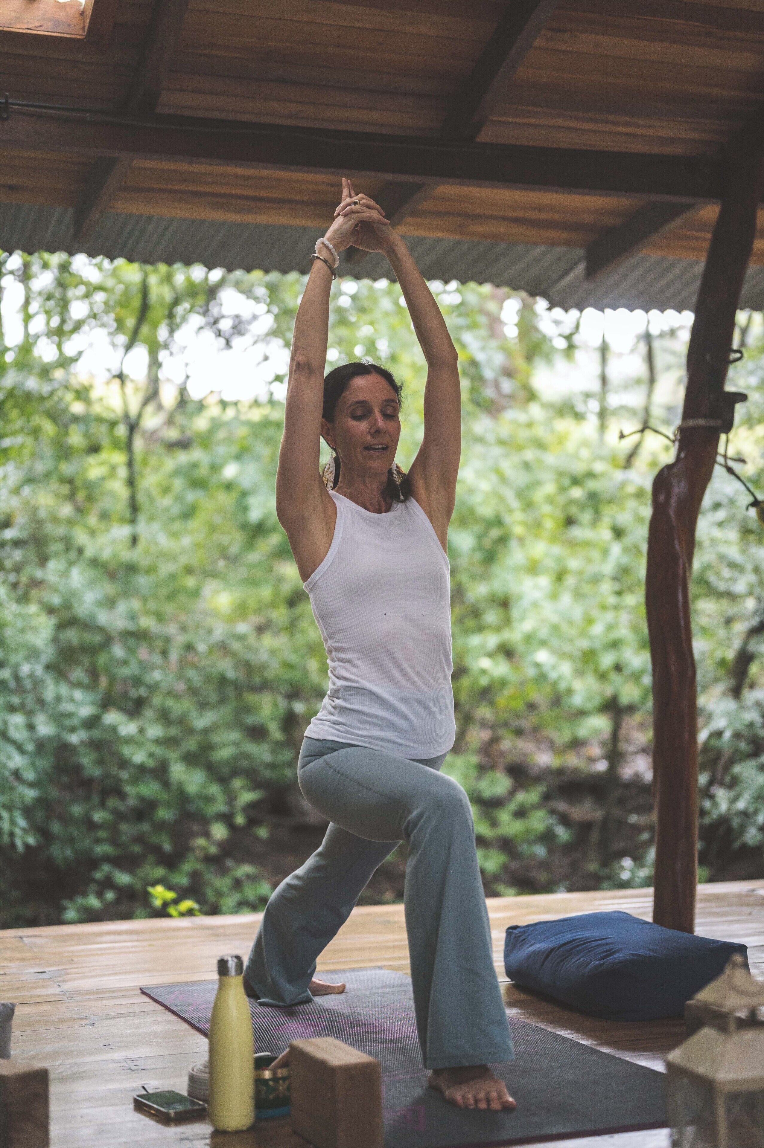 A person performing a yoga pose on a mat under a wooden structure with a natural backdrop.