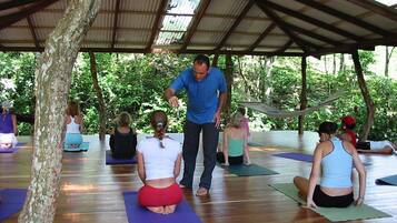 A group of people on yoga mats under a covered area with a wooden floor.