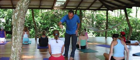 A group of people on yoga mats under a covered area with a wooden floor.