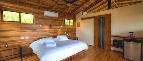 A spacious bedroom with a large bed, wooden ceiling beams, and a built-in desk with a refrigerator.