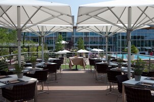 Un área de comedor al aire libre con mesas y sillas, sombrillas y una piscina al fondo.