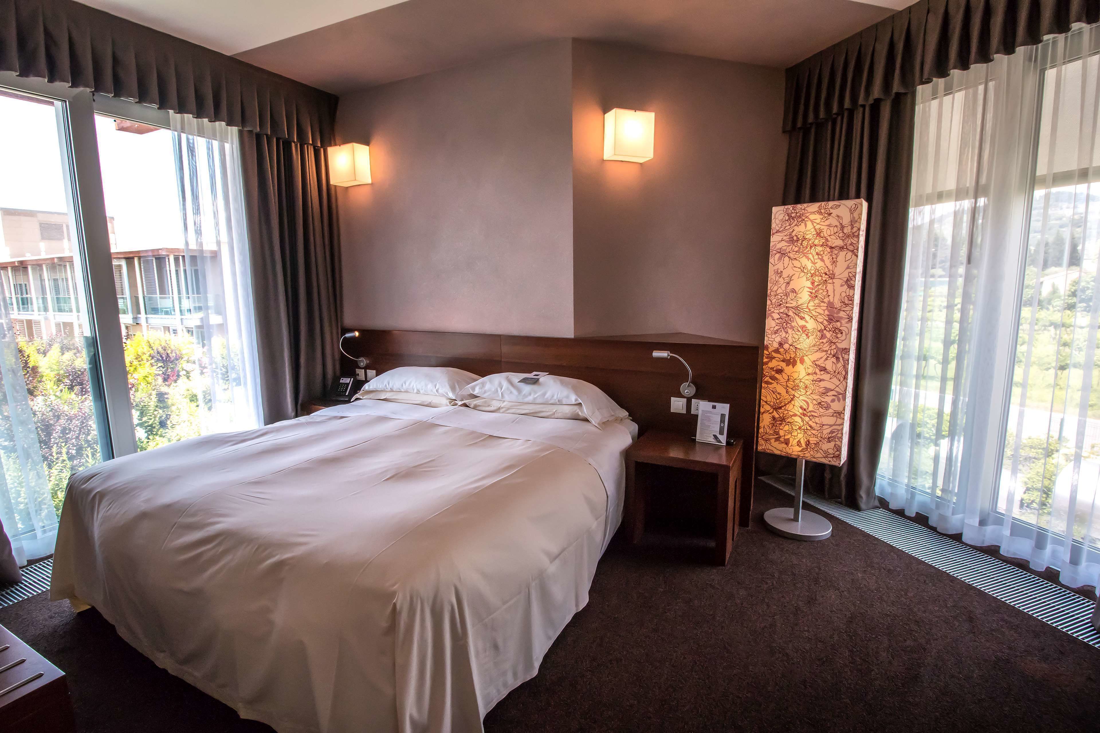 A hotel room with a large bed, two bedside lamps, a nightstand, and a floor lamp.