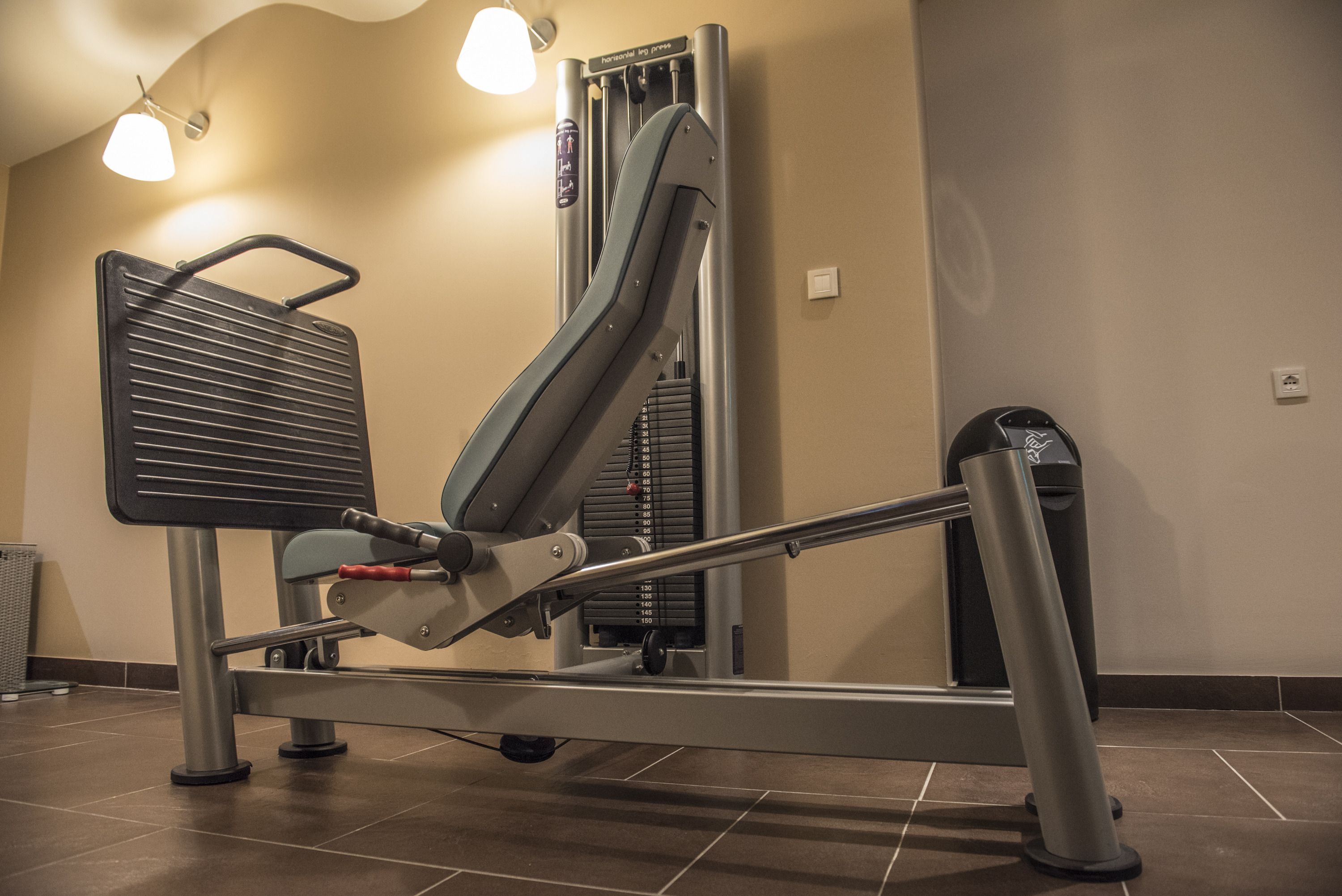Una máquina de remo en un gimnasio, con una pantalla montada en la pared y un cubo de basura.