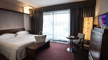 Une chambre d’hôtel équipée d’un lit, d’un bureau, d’une chaise, d’une télévision et d’une fenêtre avec des rideaux.