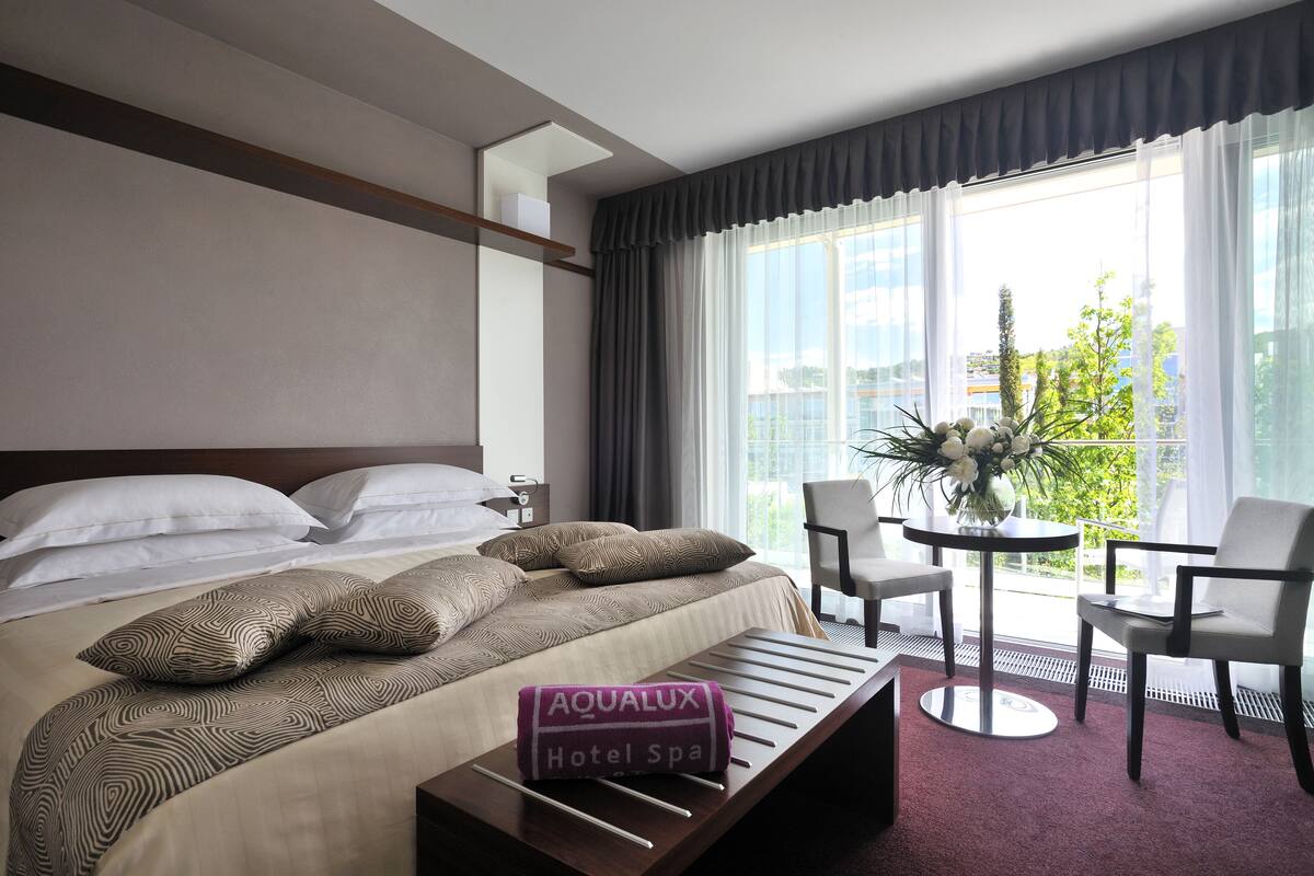 Quarto de hotel com cama, mesa pequena com toalha e varanda com cadeiras e mesa.