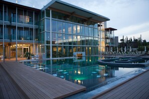 A modern hotel with a glass facade, a pool area, and outdoor seating.