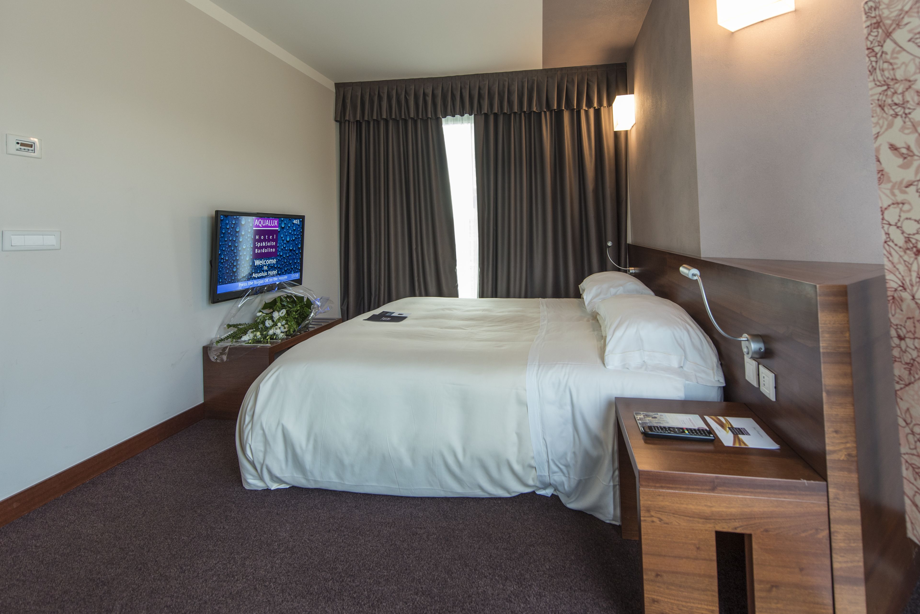 A hotel room with a bed, bedside table, TV, and a window with curtains.