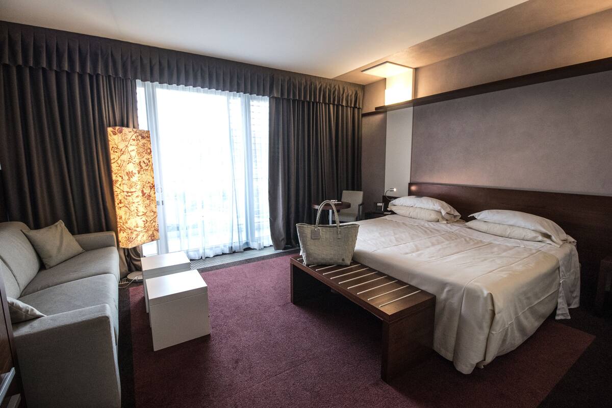 Quarto de hotel com cama, sofá, escrivaninha e luminária.