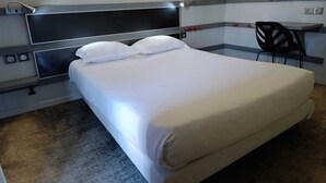 A hotel room with a bed, a chair, a desk, and a wall-mounted rack with hangers. - Enzo Trappes by Kyriad Direct (Trappes)