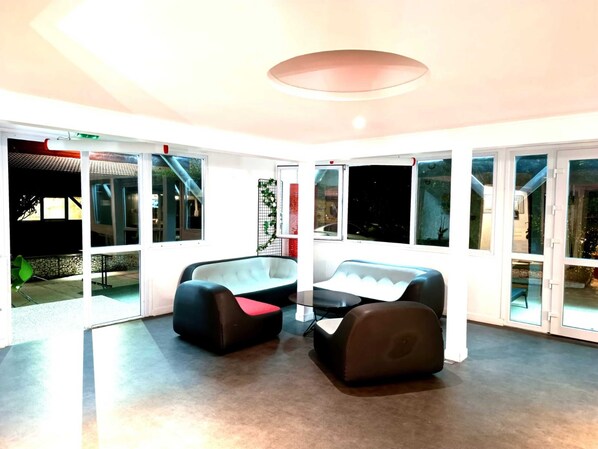 En rummelig stue med store vinduer, en moderne loftlampe og et siddeområde med et bord.