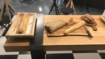 Un comedor con piso a cuadros, una mesa de madera con pan y un cuchillo, y sillas negras.