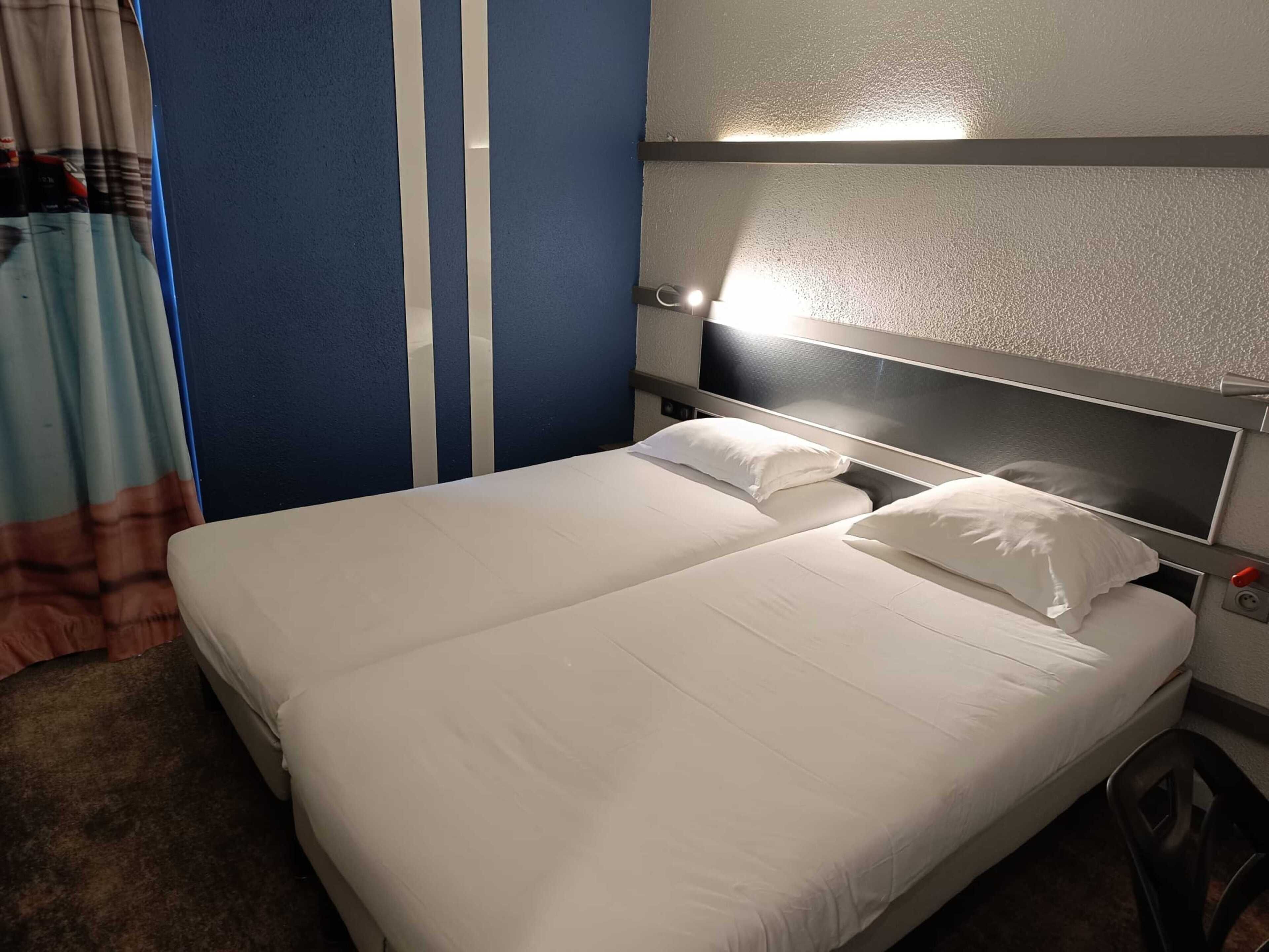 Une chambre d’hôtel avec un lit, une tête de lit dotée d’une lampe et un rideau.