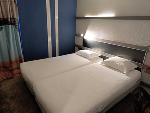 Una habitación de hotel con una cama, un cabecero con luz y una cortina.