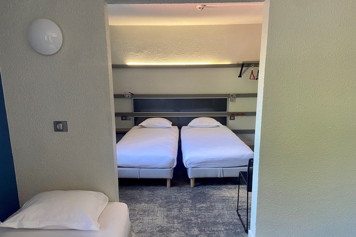 A hotel room with two beds, a carpeted floor, a light fixture, and a wall-mounted light.