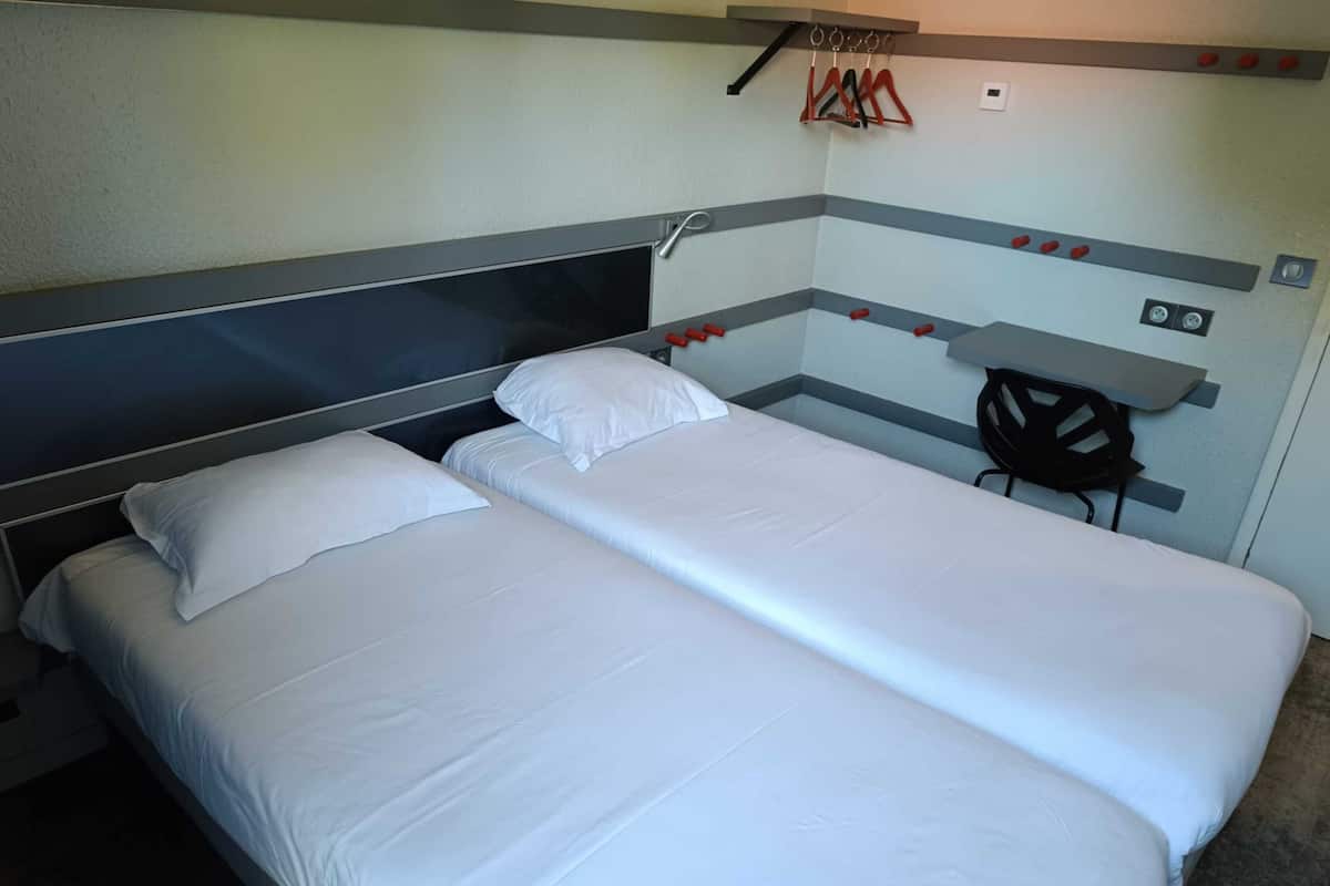 A hotel room with two beds, a desk, and a chair.